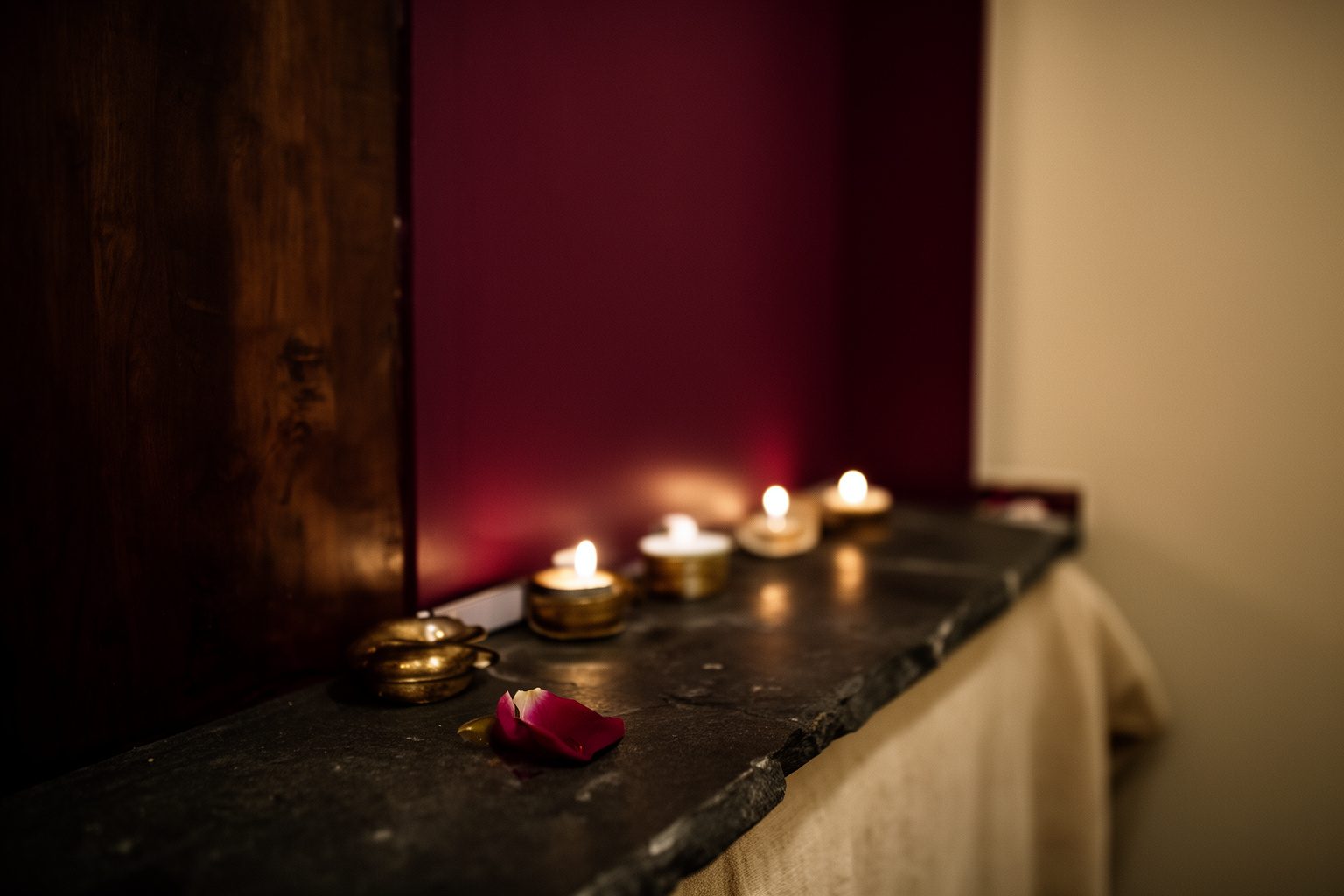 Fila de velas pequenas numa laje de pedra escura, com uma pétala caída