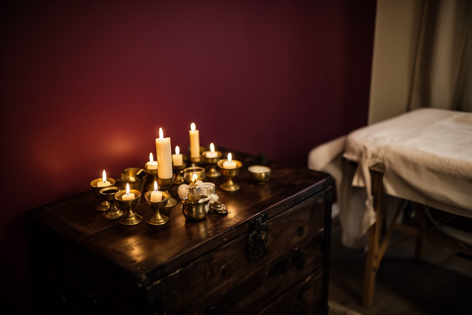 Conjunto de velas em pequenos castiçais de latão sobre um baú de madeira escura